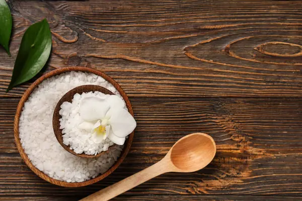 Kase dolusu deniz tuzu, orkide çiçeği ve tahta arka planda kaşık kompozisyonu