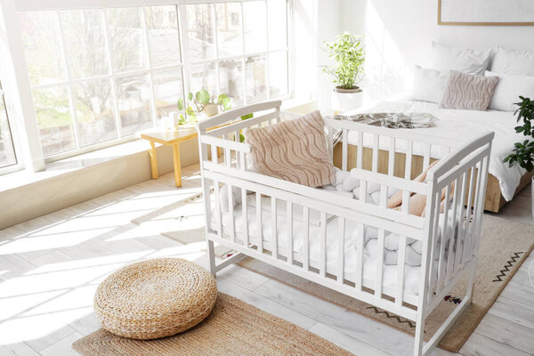 Interior of light room with bed, baby crib and window