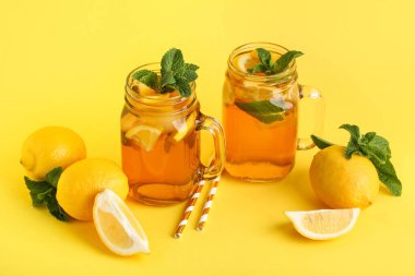 Sarı arka planda nane ve narenciye içeren limonlu buzlu çay kavanozları.