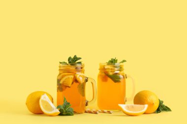 Sarı arka planda nane ve narenciye içeren limonlu buzlu çay kavanozları.