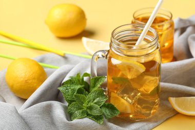 Mason kavanozu ve bir bardak limonlu buzlu çay, sarı arka planda naneli, yakın plan.