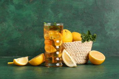 Yeşil zemin üzerinde nane ve narenciye meyveli bir bardak buzlu limon çayı.