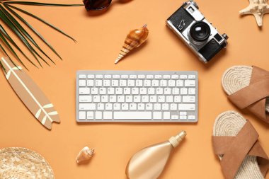 Kamera ve turuncu arka planda plaj aksesuarları olan bilgisayar klavyesi