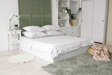 Beyaz çarşaflı, beyaz perdeli ve dolabı olan ışık odasının içinde.