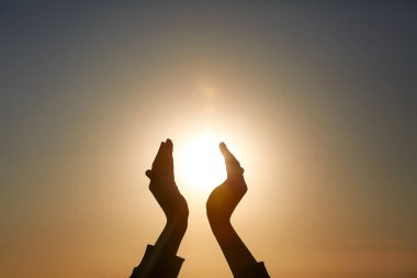 Gün batımında güneşi tutan kadın ellerinin silueti. Yaz gündönümü