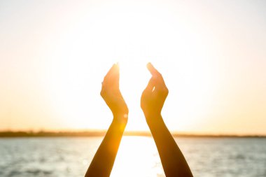 Gün batımında güneşi nehre karşı tutan kadın ellerinin silueti. Yaz gündönümü