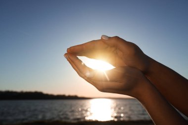 Gün batımında güneşi nehre karşı tutan kadın eller. Yaz gündönümü