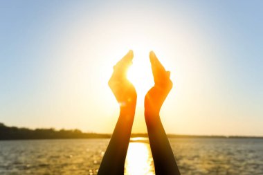 Gün batımında güneşi nehre karşı tutan kadın eller. Yaz gündönümü