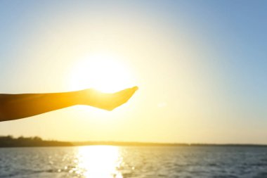 Gün batımında güneşi nehre karşı tutan kadın eli silueti. Yaz gündönümü