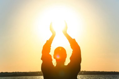 Gün batımında güneşi nehre karşı tutan bir kadın silueti. Yaz gündönümü