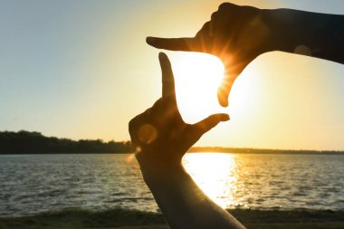 Kadın eli silueti gün batımında nehre karşı çerçeve hareketi yapıyor. Yaz gündönümü