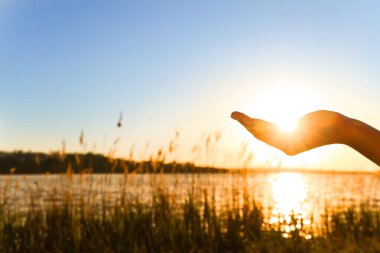 Gün batımında nehre karşı kadın eli silueti. Yaz gündönümü