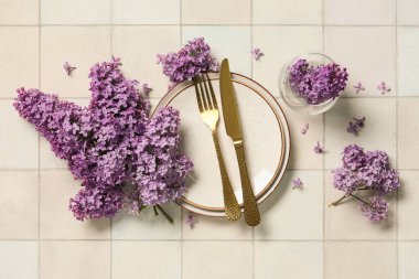 Altın çatal bıçak takımı ve beyaz fayanslı leylak çiçekleri olan güzel bir masa.