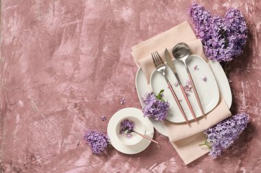 Gümüş çatal bıçak takımları ve mor arka planda leylak çiçekleri olan güzel bir masa.