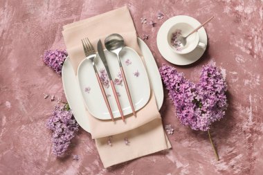 Gümüş çatal bıçak takımları ve mor arka planda leylak çiçekleri olan güzel bir masa.