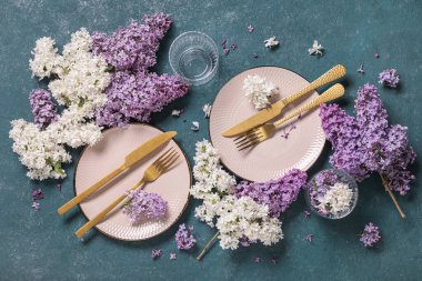 Altın çatal bıçak takımı ve yeşil arka planda leylak çiçekleri olan güzel bir masa.