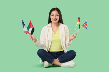 Yeşil arka planda farklı ülkelerin bayrakları olan genç Asyalı kadın.