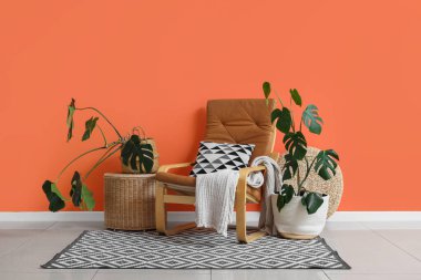 Turuncu duvarın yanında Monstera bitkileri olan koltuklar ve sepetler.