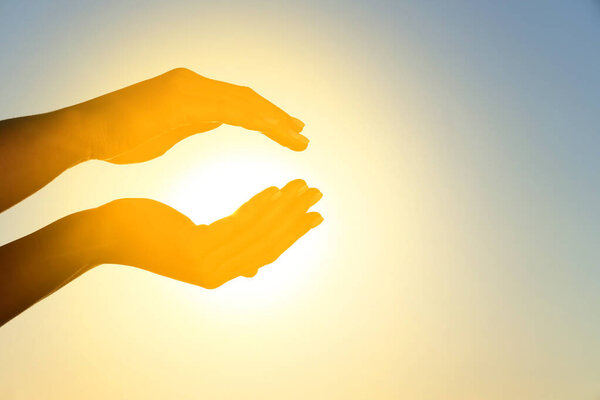 Силуэт женских рук, держащих солнце на закате. Летнее солнцестояние