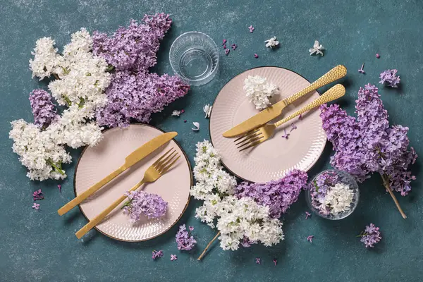 Altın çatal bıçak takımı ve yeşil arka planda leylak çiçekleri olan güzel bir masa.