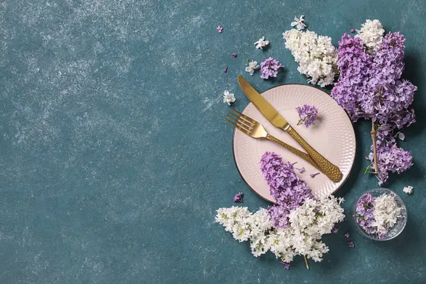 Altın çatal bıçak takımı ve yeşil arka planda leylak çiçekleri olan güzel bir masa.