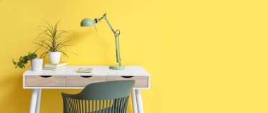 Sarı duvarın yanında çiçek ve masa lambası olan masa.