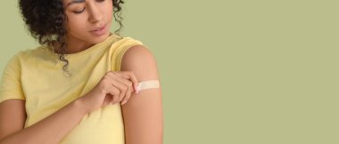 Yeşil arka planda aşıdan sonra tıbbi yaması olan genç bir Afro-Amerikalı kadın.