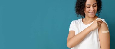 Mavi arka plandaki aşıdan sonra uygulamalı tıbbi yaması olan genç bir Afro-Amerikalı kadın.