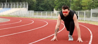 Güneş gözlüklü genç adam stadyumda koşmaya hazırlanıyor.