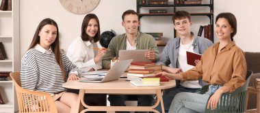 bir grup öğrenci kütüphanede masada oturuyor.