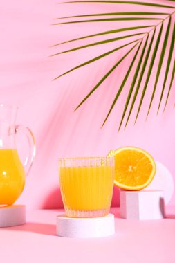 Pembe arka planda taze portakal suyu ve palmiye yaprağıyla dekoratif podyum