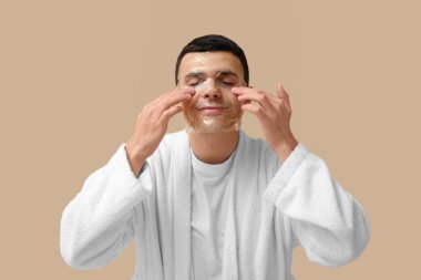 Bej arka planda yüz maskesi olan bornozlu yakışıklı genç bir adam portresi.