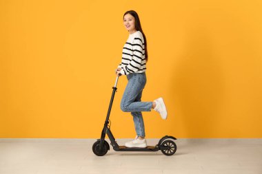 Güzel genç Asyalı kadın sarı duvarın yanında modern elektrikli scooter kullanıyor.