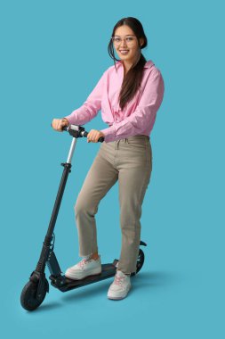 Mavi arka planda modern elektrikli scooterlı güzel bir Asyalı kadın.