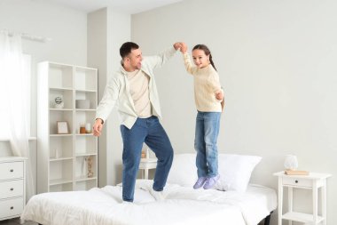 Babası ve kızı yatakta zıplıyorlar.