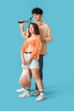 Basketbol ve tenis raketleriyle mavi arka planda şık giyinen güzel bir çift.