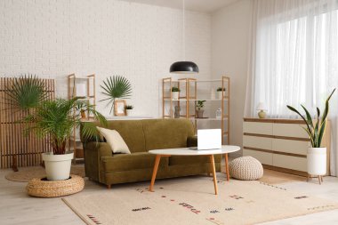 Oturma odasının içinde yeşil kanepe, bitkiler ve katlanır ekran var.