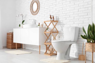 Beyaz klozet, raf ünitesi ve lavabolu çekmeceler tuvalette beyaz duvarın yanında.