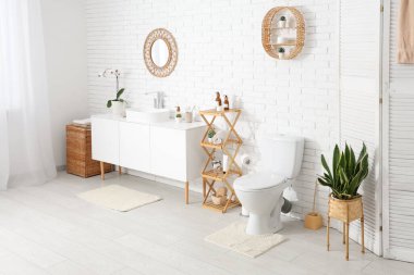 Beyaz klozet, raf ünitesi ve lavabolu çekmeceler tuvalette beyaz duvarın yanında.