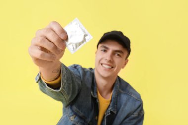 Sarı arka planda prezervatif gösteren genç adam, yakın plan.