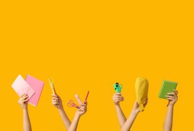 Sarı arka planda farklı kırtasiye malzemesi olan kadın elleri