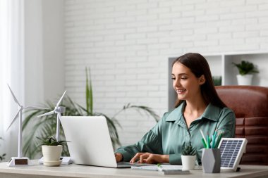 Ofisteki masada dizüstü bilgisayar ve rüzgar türbinleriyle çalışan kadın mühendis.
