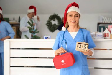 Noel Baba şapkalı olgun bir bayan doktor. İlk yardım çantası ve küp takvimi ile Noel arifesinde hastanede.