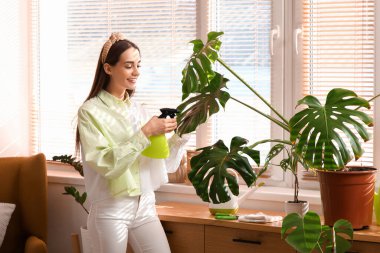 Evdeki çiçeklere su püskürten güzel genç bir kadın.