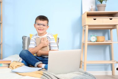 Yatak odasında kitap okuyan sevimli küçük bir çocuk.