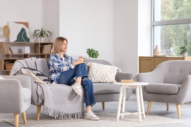 Evdeki kanepede bir fincan çayla dinlenen genç bayan.