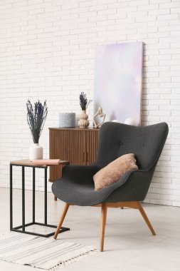 Dekorlu ahşap dolap, poster, lavanta çiçekleri ve hafif tuğla duvarın yanındaki rahat koltuk.