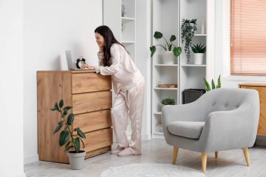 Çizgili pijamalı kadın evde klozette dizüstü bilgisayarla çalışıyor.