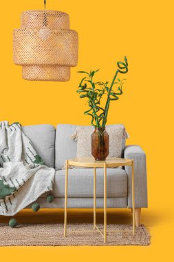 Vazoda bambu saplı masa, kanepe ve sarı arka planda lamba.
