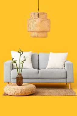 Sarı arka planda bambu saplı vazo, puf, kanepe ve lamba.